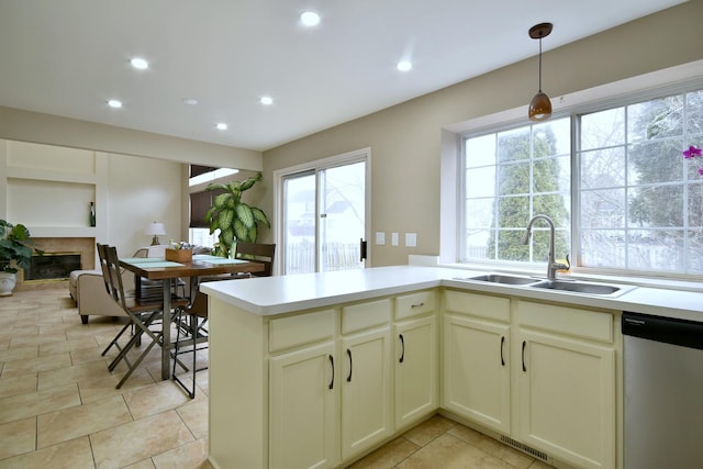 kitchen with recessed lighting, a sink, dishwasher, a glass covered fireplace, and pendant lighting