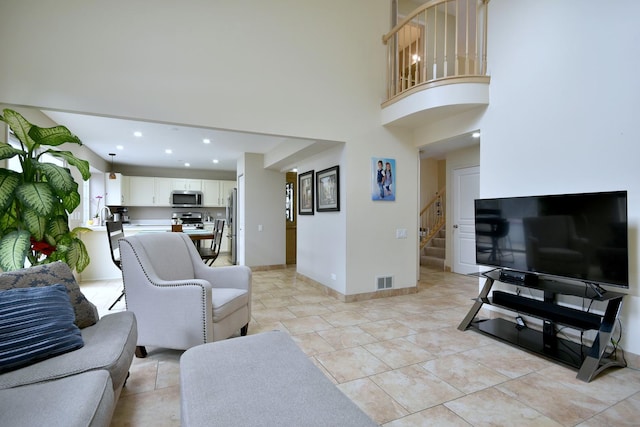 living area featuring recessed lighting, visible vents, a towering ceiling, stairs, and baseboards