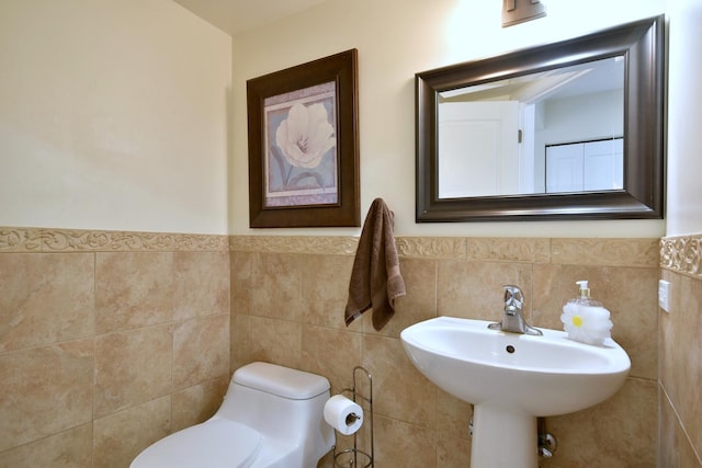 bathroom featuring toilet, tile walls, a sink, and wainscoting