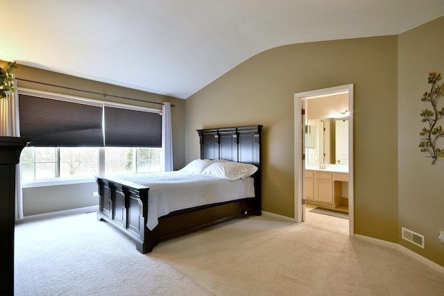 bedroom with lofted ceiling, connected bathroom, light carpet, visible vents, and baseboards