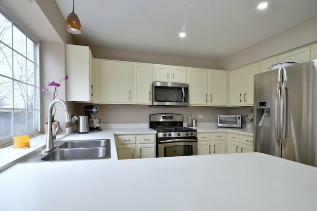 kitchen with a toaster, a sink, light countertops, appliances with stainless steel finishes, and decorative light fixtures