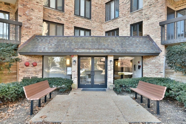 entrance to property featuring french doors, brick siding, and a shingled roof