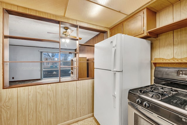 kitchen with freestanding refrigerator, wood walls, gas stove, and a ceiling fan