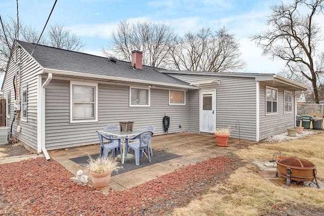 rear view of property featuring central AC unit, a fire pit, a shingled roof, a chimney, and a patio area