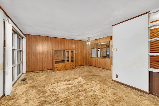 unfurnished living room with visible vents, a ceiling fan, carpet flooring, wooden walls, and baseboards