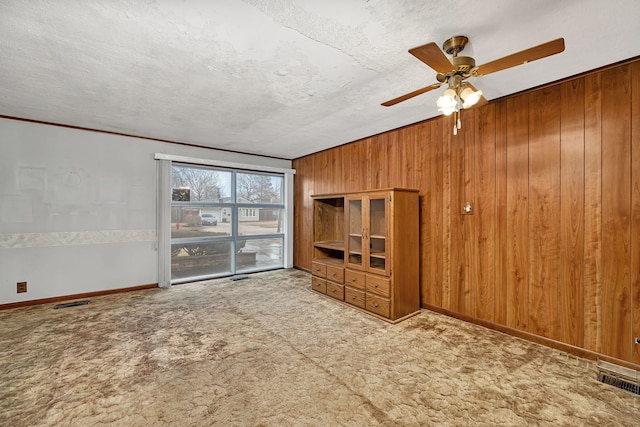 unfurnished living room featuring a textured ceiling, carpet floors, and wood walls