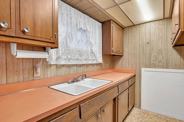 kitchen featuring brown cabinetry, light countertops, a sink, and wood walls