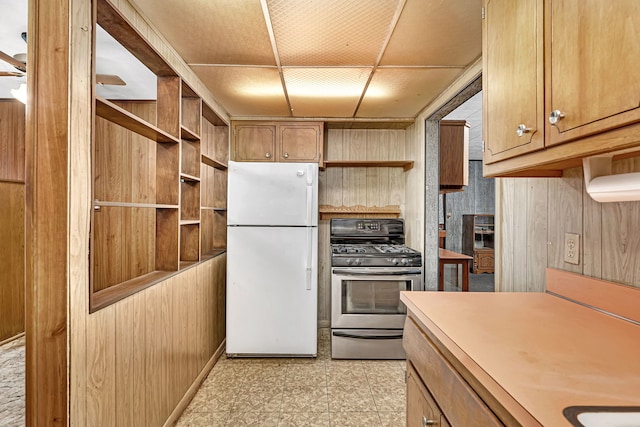 kitchen featuring light floors, open shelves, freestanding refrigerator, wood walls, and stainless steel gas range oven