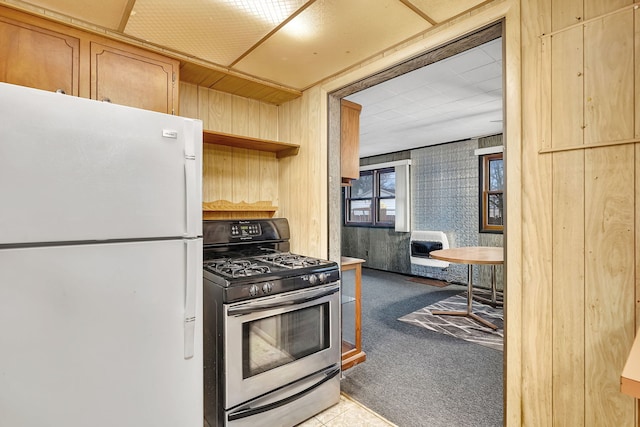 kitchen featuring stainless steel gas stove, wooden walls, freestanding refrigerator, heating unit, and carpet flooring