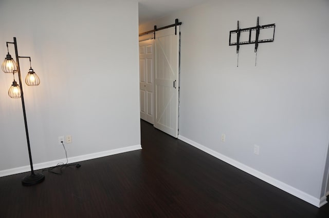 empty room with dark wood-style floors, baseboards, and a barn door