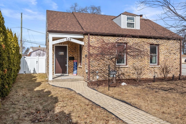 view of front of property featuring roof with shingles, a gate, fence, and brick siding