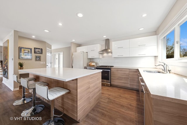 kitchen featuring stainless steel electric range oven, freestanding refrigerator, wall chimney range hood, and modern cabinets