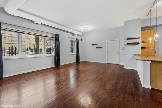 unfurnished living room featuring track lighting, baseboards, a sink, and wood finished floors