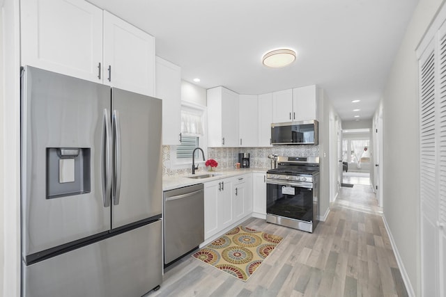 kitchen featuring stainless steel appliances, tasteful backsplash, light countertops, white cabinetry, and a sink