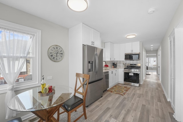 kitchen with light wood finished floors, stainless steel appliances, light countertops, white cabinetry, and backsplash