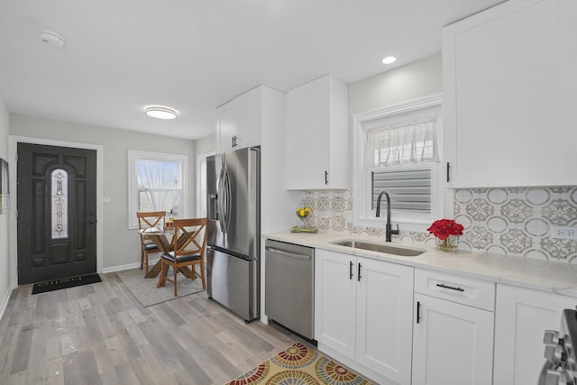 kitchen featuring tasteful backsplash, appliances with stainless steel finishes, light wood-style floors, white cabinets, and a sink