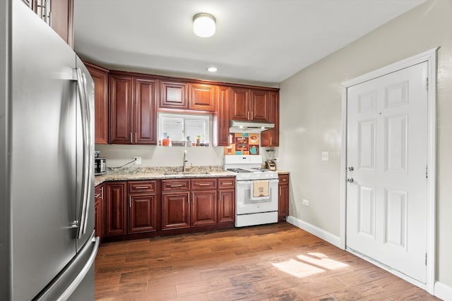 kitchen featuring a sink, under cabinet range hood, wood finished floors, freestanding refrigerator, and white range with gas stovetop