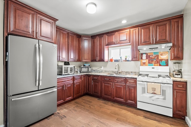 kitchen with under cabinet range hood, light wood-type flooring, white range with gas cooktop, freestanding refrigerator, and a sink