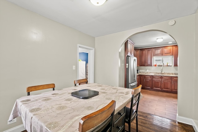 dining room with arched walkways, dark wood finished floors, and baseboards