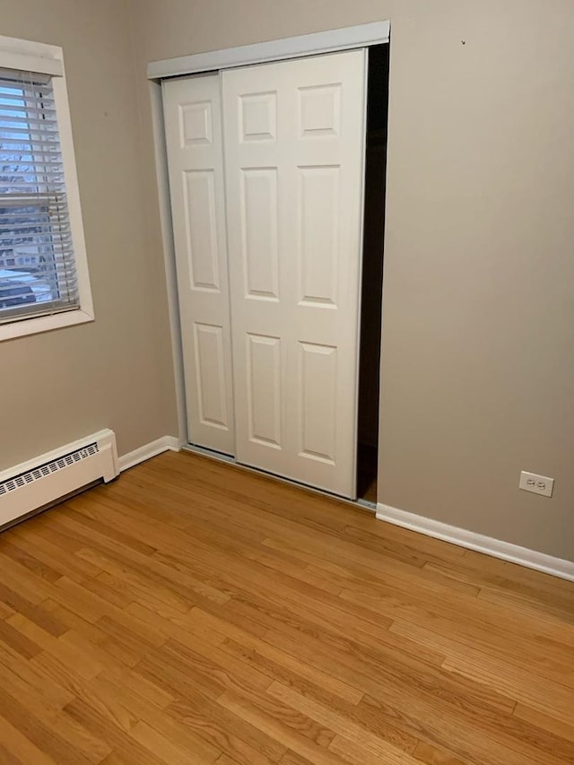 unfurnished bedroom featuring light wood-style flooring, baseboards, baseboard heating, and a closet