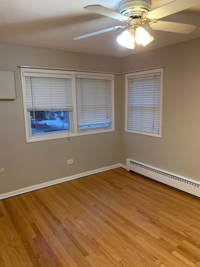 empty room with light wood-style floors, a baseboard radiator, ceiling fan, and baseboards