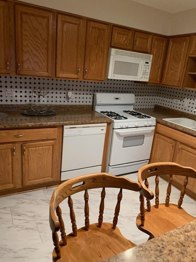 kitchen with white appliances, a sink, marble finish floor, brown cabinets, and tasteful backsplash