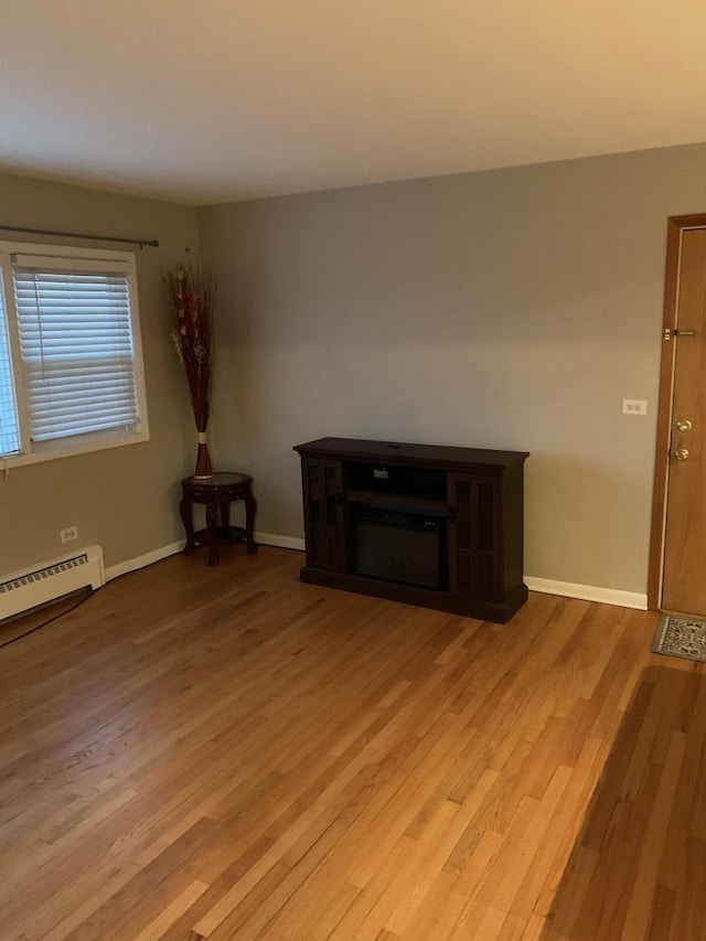 interior space with a baseboard heating unit, light wood finished floors, a fireplace, and baseboards