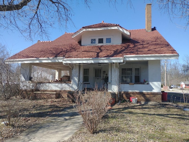 view of front facade featuring an attached carport, covered porch, a tile roof, stucco siding, and a chimney