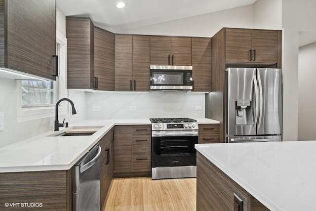 kitchen with light wood-style floors, decorative backsplash, stainless steel appliances, and a sink