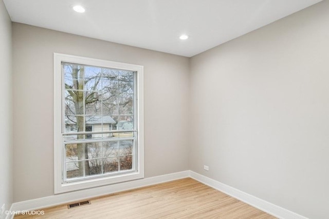 empty room featuring a wealth of natural light, light wood-style flooring, visible vents, and baseboards