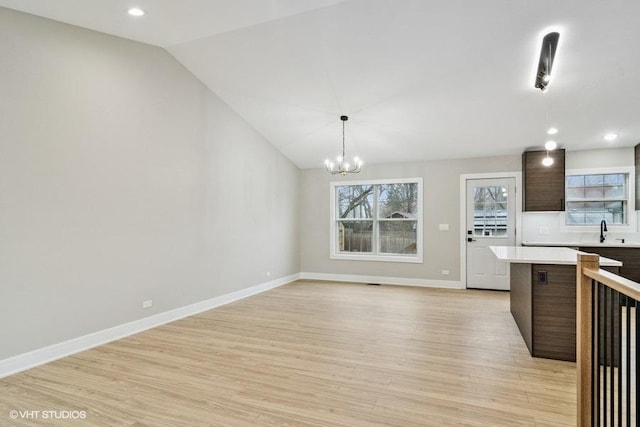 kitchen with decorative light fixtures, light wood finished floors, lofted ceiling, light countertops, and baseboards