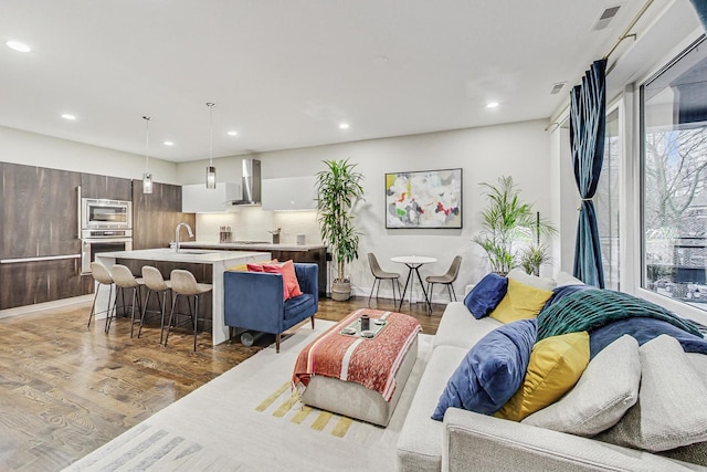 living area with recessed lighting, visible vents, light wood-style flooring, and baseboards