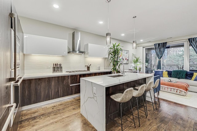 kitchen with light wood-style floors, a sink, wall chimney range hood, and modern cabinets