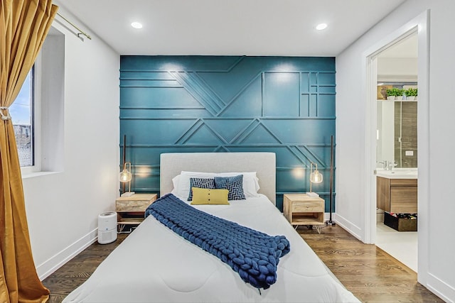 bedroom with baseboards, dark wood finished floors, an accent wall, ensuite bathroom, and a decorative wall