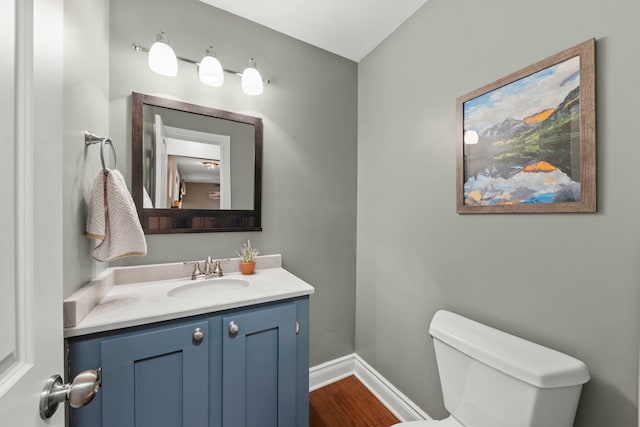 half bathroom featuring toilet, vanity, baseboards, and wood finished floors