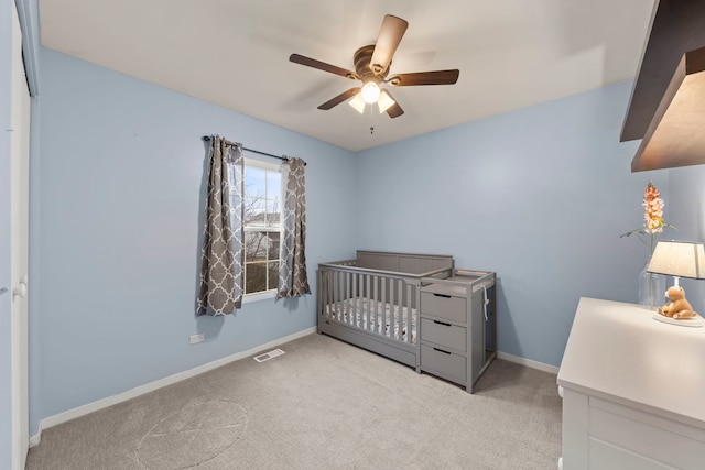 carpeted bedroom with a ceiling fan, visible vents, a crib, and baseboards