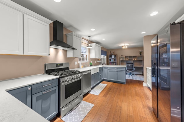 kitchen with recessed lighting, appliances with stainless steel finishes, light wood-style floors, white cabinetry, and wall chimney range hood