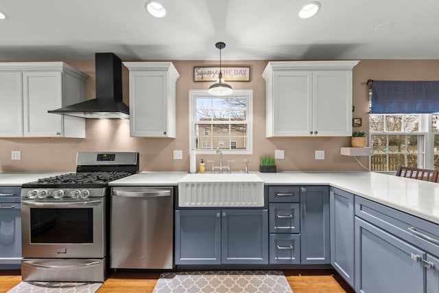 kitchen with wall chimney range hood, appliances with stainless steel finishes, light countertops, and a sink