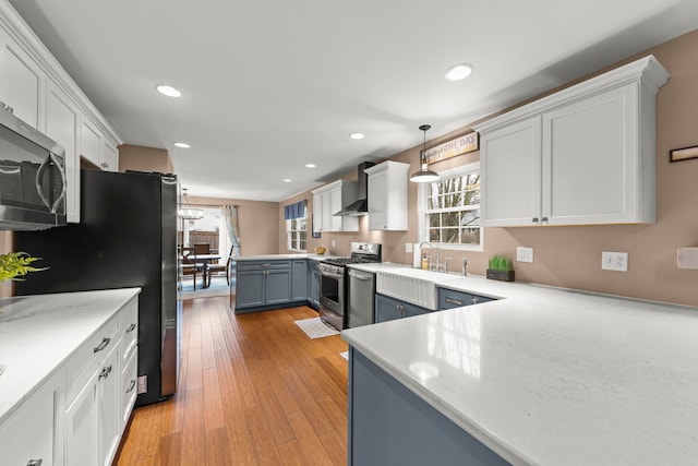 kitchen featuring stainless steel appliances, a sink, a healthy amount of sunlight, light wood-style floors, and wall chimney range hood