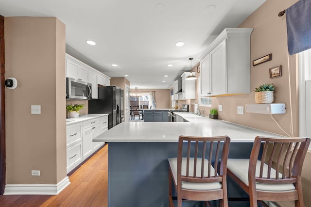 kitchen with stainless steel appliances, a peninsula, a sink, light countertops, and light wood finished floors