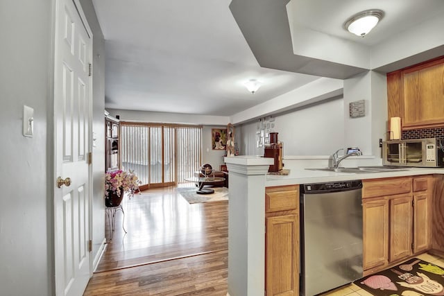 kitchen featuring brown cabinets, stainless steel dishwasher, light wood-style floors, a sink, and a peninsula