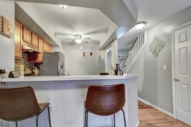 kitchen featuring ceiling fan, under cabinet range hood, light wood-type flooring, tasteful backsplash, and stainless steel fridge