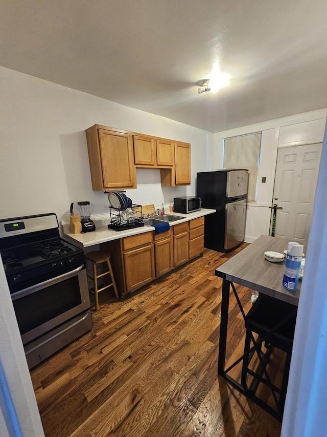 kitchen featuring appliances with stainless steel finishes, dark wood-style flooring, light countertops, and a sink