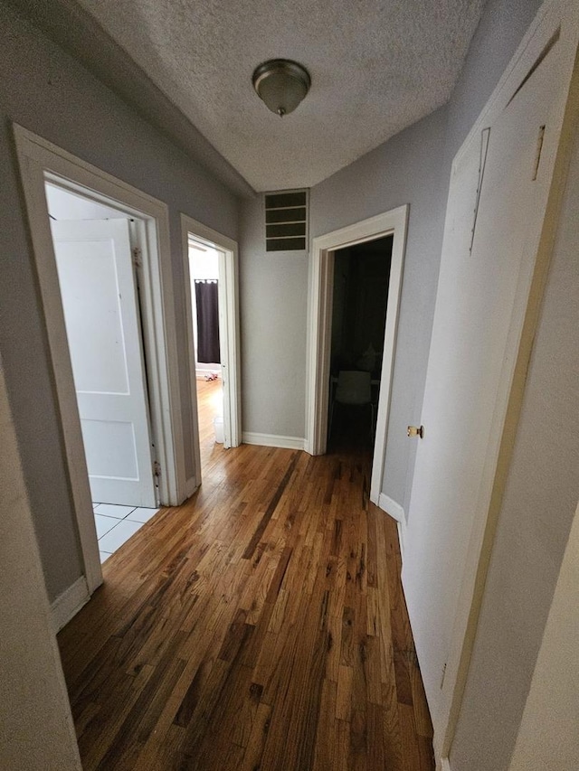 corridor featuring baseboards, a textured ceiling, visible vents, and hardwood / wood-style floors