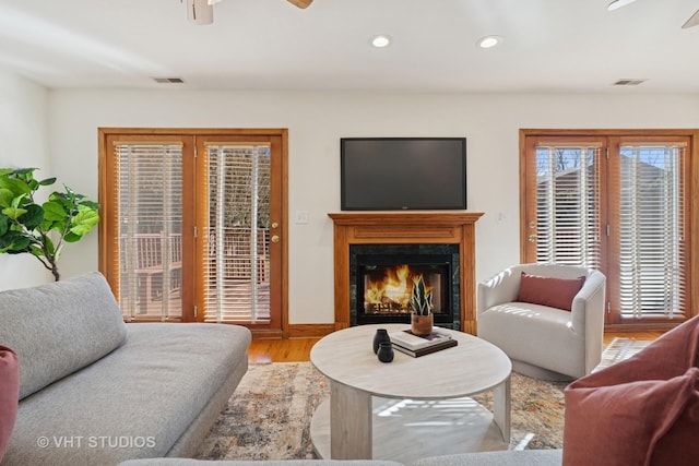 living area featuring visible vents, a warm lit fireplace, ceiling fan, and wood finished floors