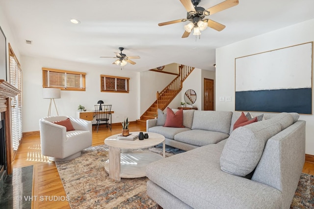 living room featuring stairway, wood finished floors, visible vents, a fireplace, and ceiling fan