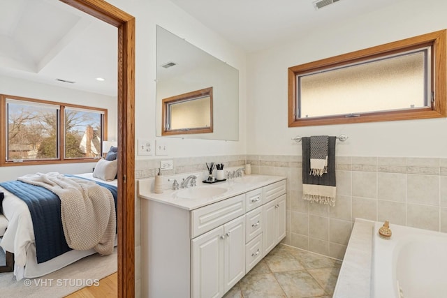 ensuite bathroom featuring visible vents, ensuite bathroom, a sink, tile walls, and double vanity