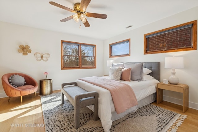 bedroom with ceiling fan, visible vents, baseboards, and wood finished floors