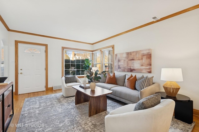 living room with visible vents, light wood-type flooring, baseboards, and ornamental molding