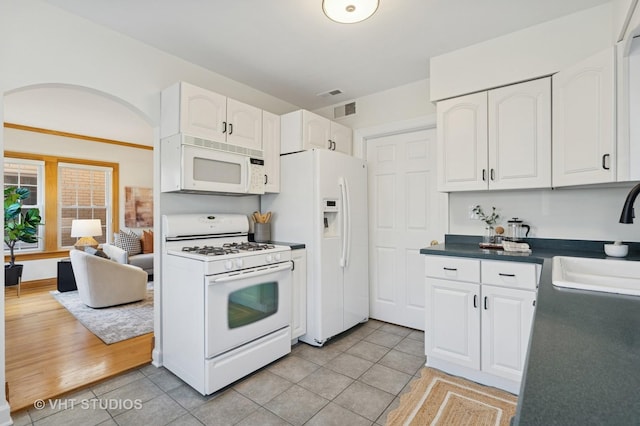 kitchen with white appliances, visible vents, a sink, white cabinets, and dark countertops